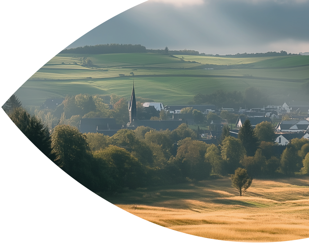 Blick auf Sankt Vith mit Kirchturm und umliegenden grünen Hügeln.