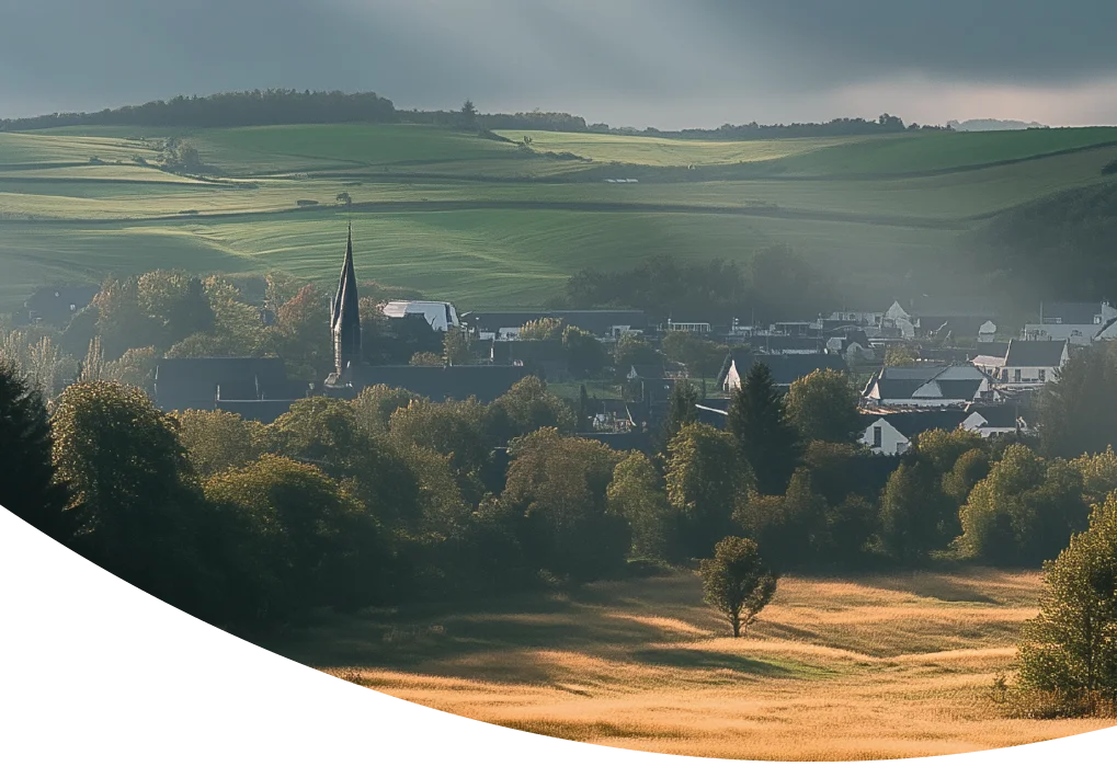 Blick auf Sankt Vith mit Kirchturm und umliegenden grünen Hügeln.