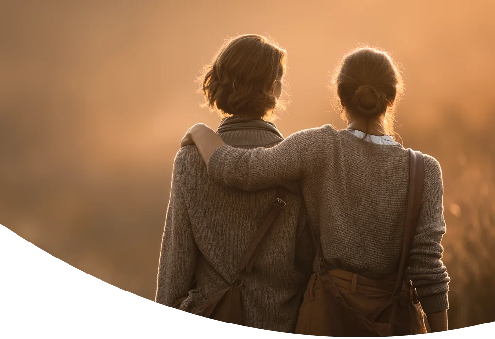 Zwei Frauen im warmen Abendlicht, eine legt der anderen den Arm um die Schulter.